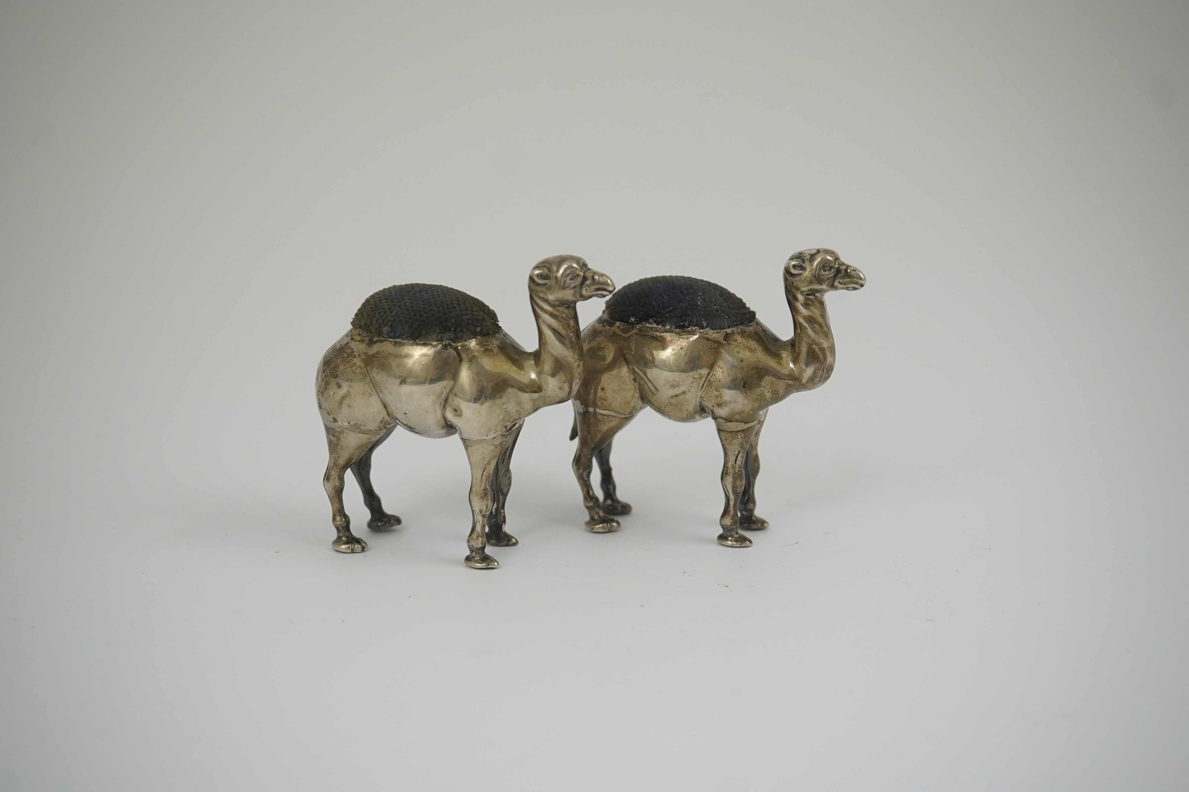 A pair of Edwardian novelty silver pin cushions, each modelled as a camel